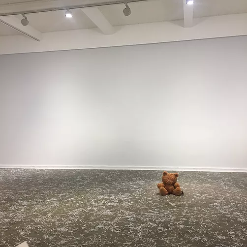 a brown classic teddy bear with no eyes sits on the floor amongst the shredded paper