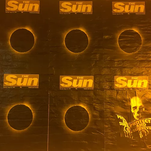the wall is plastered with posters of the sun newspaper but the page is totally blacked out and there&rsquo;s an eclipse on it, as in, an eclipse of the sun newspaper