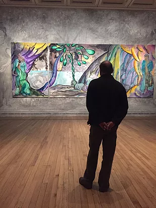 a man stands and looks at the paintings, which show a watery island and a palm tree with smooth shapes and black outlines