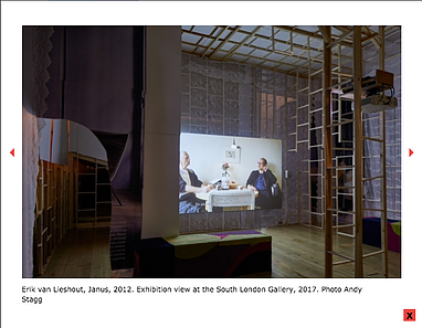 an installation shot of a wooden structure with a projection inside of it of two people a a table with a flower in the middle of them