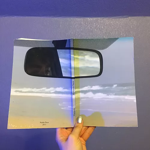 Gab holds the book up so that both of the pages can be seen, and it&rsquo;s a washed out coast with big waves while the rear view mirror can be seen at the top of the spread