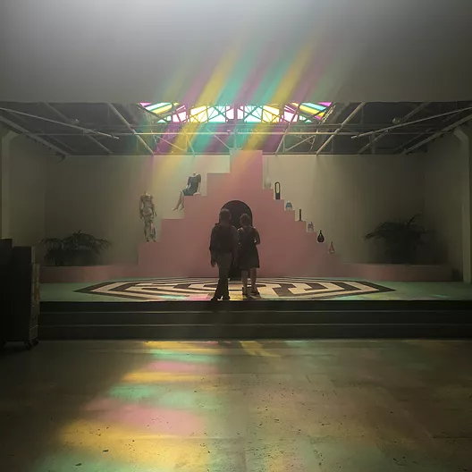 sunlight through stained glass glows down onto the gallery floor, where there is a pink pyramid and a black and white spiral set