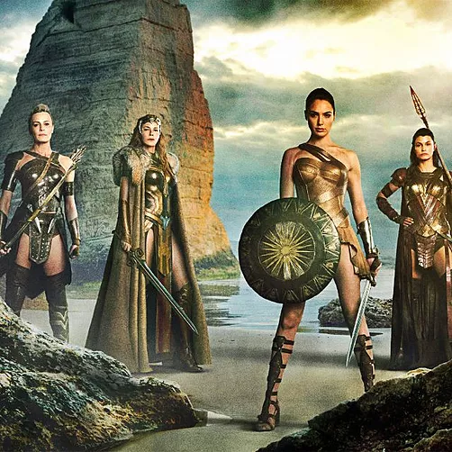 wonder woman stands with a big shield in front of her, next to the amazons, they all have swords and are standing on a beach together