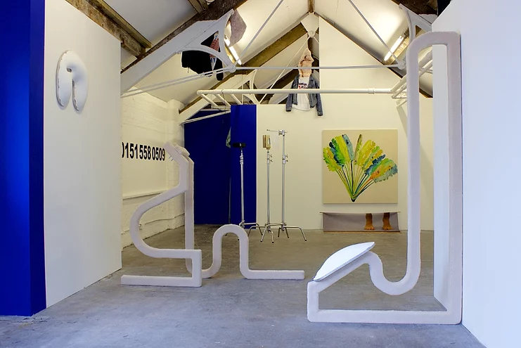 a shot of an exhibition that has a painting of palm fronds, a local 0151 phone number on the wall, yves klein blue sections on the walls, and two white bending abstract sculptures cut the space with their outlines