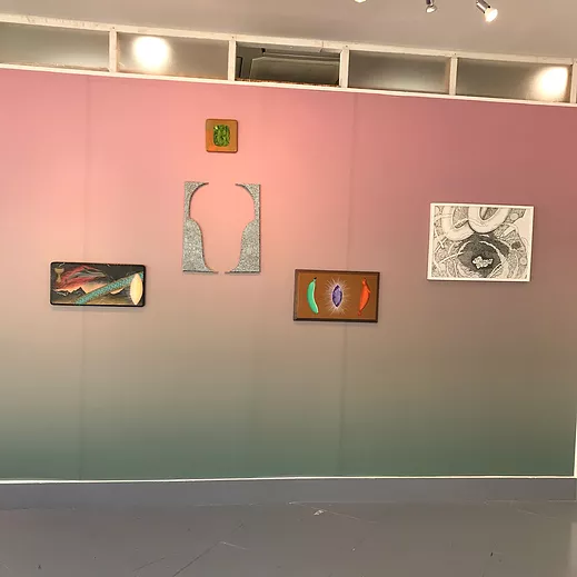 a gradient from green to pink on a gallery wall with different small paintings placed on different parts of the wall