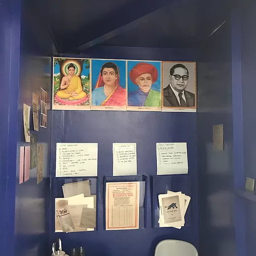 inside a blue booth, there is information leaflets, plastic containers to take information out of, and three artworks of portraits at the top of the booth
