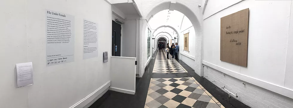 an image in the corridor in Goldsmiths, all white, tiles, a bit fancy, with info cards on the wall for the file under female exhibition. On the right wall, there is a hessian stretched over a square board and stitched on top it says &lsquo;she sits. fleeting in a single pocket cellulose acetate