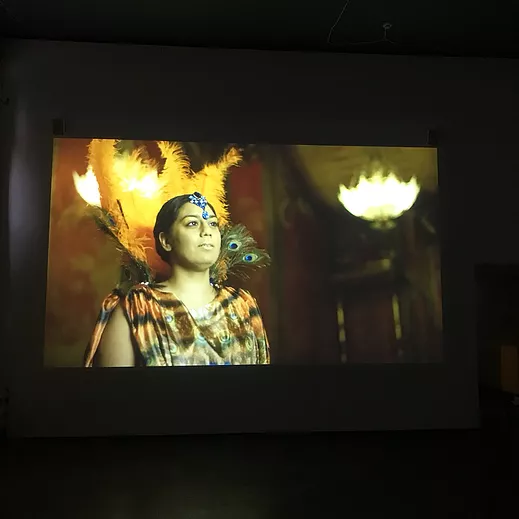 a woman with feathers and peacock feathers around her head stands looking past the camera with jewellery down from her hairline across his forehead