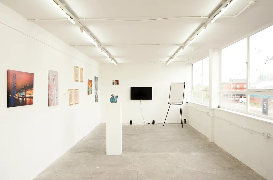 a shot of the exhibition in a white cube space with paintings and framed photos on the walls, and there&rsquo;s a plinth in the centre with a blue wizard on it