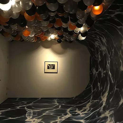 the wave pattern gallery floor stretches up so that it becomes the wall and then the ceiling in a big curve, and on the ceiling there are black silver white and orange balloons