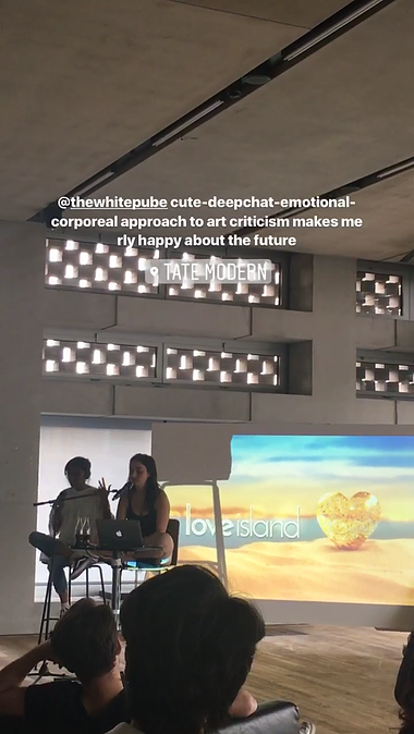 a shot of Gabrielle and Zarina on stools with a projection behind them of an episode of love island while they give a lecture