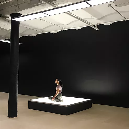 a performer is sat on a huge lightbox with their legs to the side