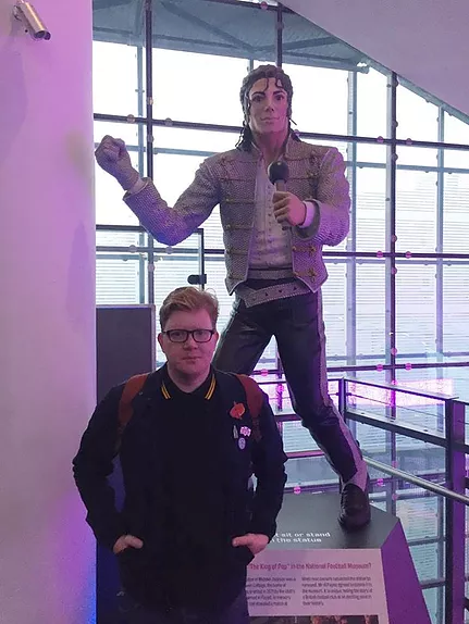 GT stands with his hands in his pockets in front of a bad michael jackson statue