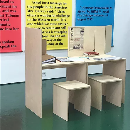 a tiny wooden makeshift desk with two stools like a little workstation for kids is situated in front of the colourful banners