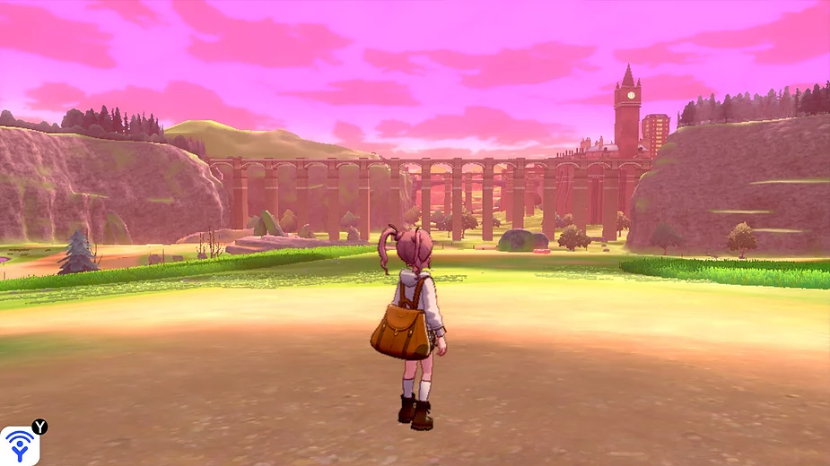 a white girl with pink hair in pigtails stands with a chunky satchel backpack on looking out over fields and bridges and a tower in the background below a pink twilight sky