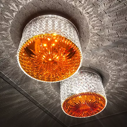 a crystal ceiling light in an amber colour is hung from the office ceiling squares and casts out reflections in diamond shapes onto the rough pattern