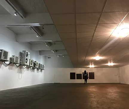 the white cube gallery space has a lowered ceiling on one end made up of those squares that office ceilings often have, and on the other side there is a row of outdoor air conditioners