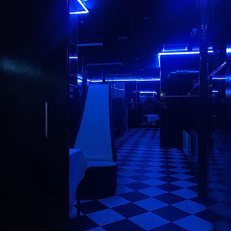 the inside of a strip club which is dark, blue lights, and black and white tiled diamond floor