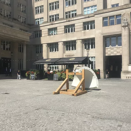 a big white curved sculpture is held up with a wooden frame in public space