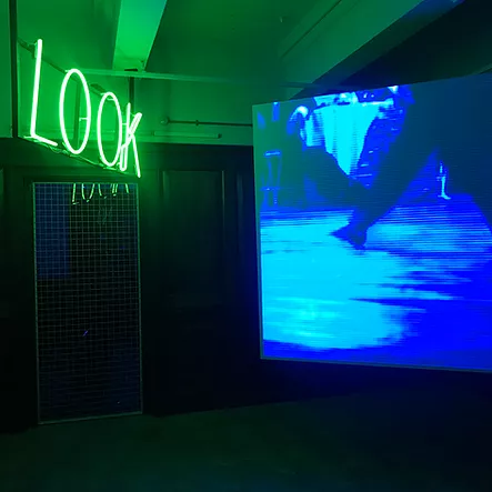 a blue tinted video of someone&rsquo;s legs as they dance and in green neon opposite is the word LOOK