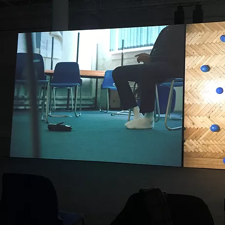 a man has his shoes off showing white socks on a teal floor amongst blue chairs