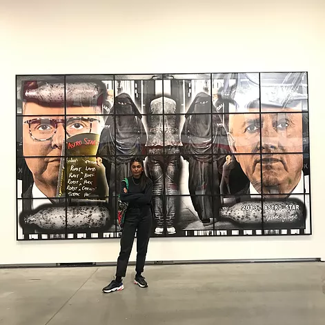 Zarina stands pissed off in front of another art work that has the artists own faces huge in colour either side of a mirrored image of a woman in hijab