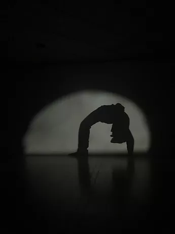 a black shadow of a child doing the crab under a spotlight is projected on a wall