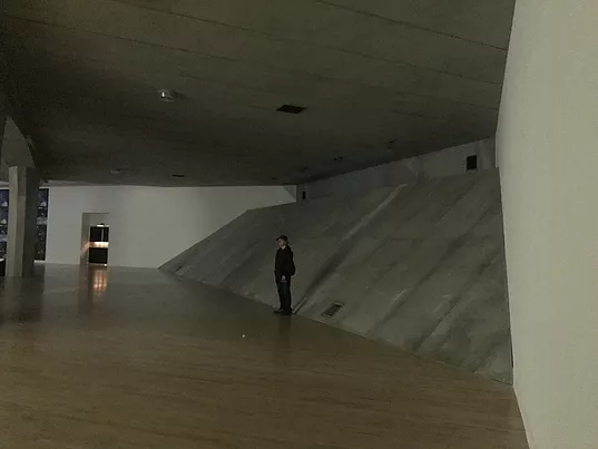 a gallery visitor stands at the edge of the sloping corner to show the scale of it