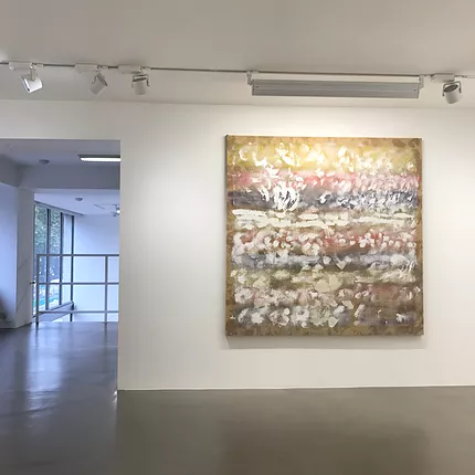 a big square painting hangs in a white cube gallery space, and it is like very pale strips of pastel colours in the background with repeated white blurred circles and other marks on top all the way across and down