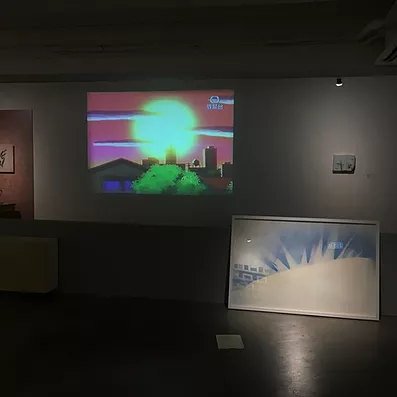 theres an abstract white and blue framed image on the floor propped against a very low gallery wall, and then behind that a projection on the wall of a sun in anime