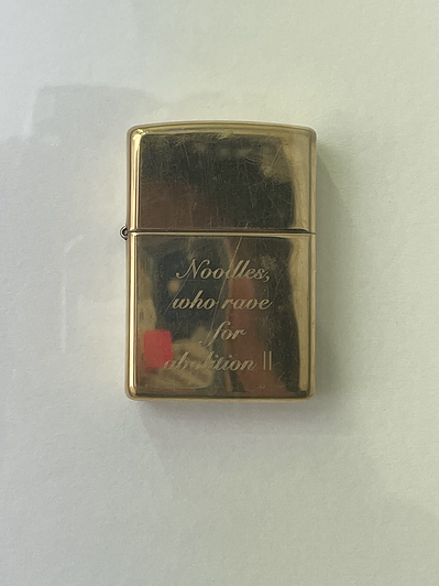a gold lighter has words carved onto it, saying Noodles, who rave for abolition