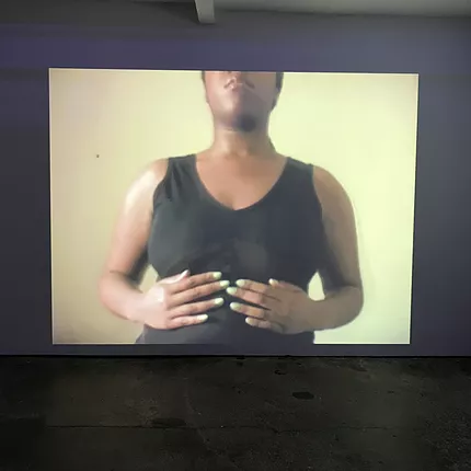 a black person stands with a tank top on with their hands below their chest and light green nail varnish on that almost matches the background