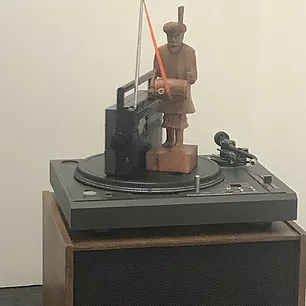 a vinyl record player has a small radio on top and a wooden figure of a man holding a drum