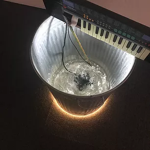 a metal bin has water bubble at the bottom of it, and over the top there is a keyboard balancing on the edges
