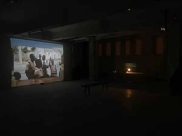 a projection in a big cement gallery space shows a group of black children