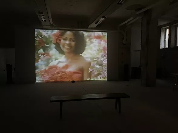 a huge projection shows a black women smiling framed by red flowers and greenery and she has one of the flowers in her hair
