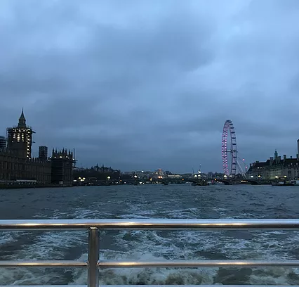 A shot of the thames from a boat showing the london eye on one side and big ben covered in scaffolding on the other bank