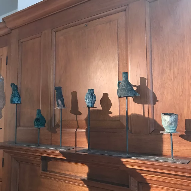small jug shaped sculptures on metal stands are in a row at different heights in a gallery with wooden walls