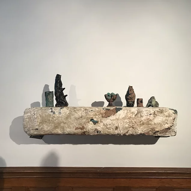 a small crusty plaster shelf on a wall holds different items on top, tiny, different shapes, nothing specific or recognisable