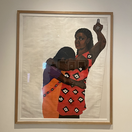 a framed painting on a wall shows to brown people, one with their head in the other ones chest, and the other has her head high looking at the viewer with one hand in the air