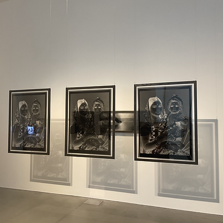 three black and white images hang in space with the shadows of the images behind them cast onto the wall: they show the film negatives of two people, it&rsquo;s hard to see clearly who they are because of the negative colouring, but it looks like a woman and a child