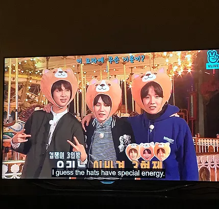 the BTS boys, three of them are wearing big hats with teddy bears on top, and the caption says I guess the hats have special energy
