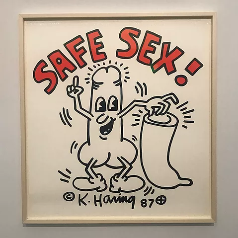 a drawing of a penis with arms and legs holding a condom and smiling below the words SAFE SEX ! in bright red