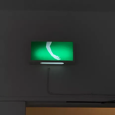 a green lit up sign on the wall where it would usually say exit but instead there is an arm hanging down with fingers loose