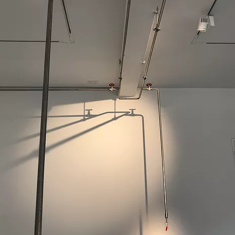 a close up of pipes along a white wall, shadows of the pipes cast down