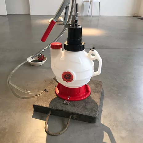 a plastic container on the floor that is in a rounded teapot shape with a handle at the side and tubes coming out of it in white red and black