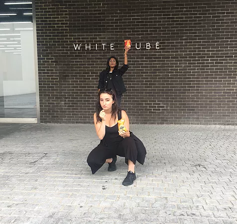 Gabrielle and Zarina are posing outside the White Cube gallery in south london, Gabrielle in front crouching on the floor eating mini cheddars, and Zarina is in the back holding Hula Hoops above the C in Cube so that it looks like the white pube hehe