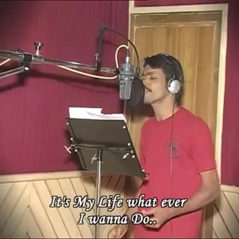 a brown man stands in a recording studio with his eyes closed singing &lsquo;it&rsquo;s my life what ever I wanna do&rsquo;