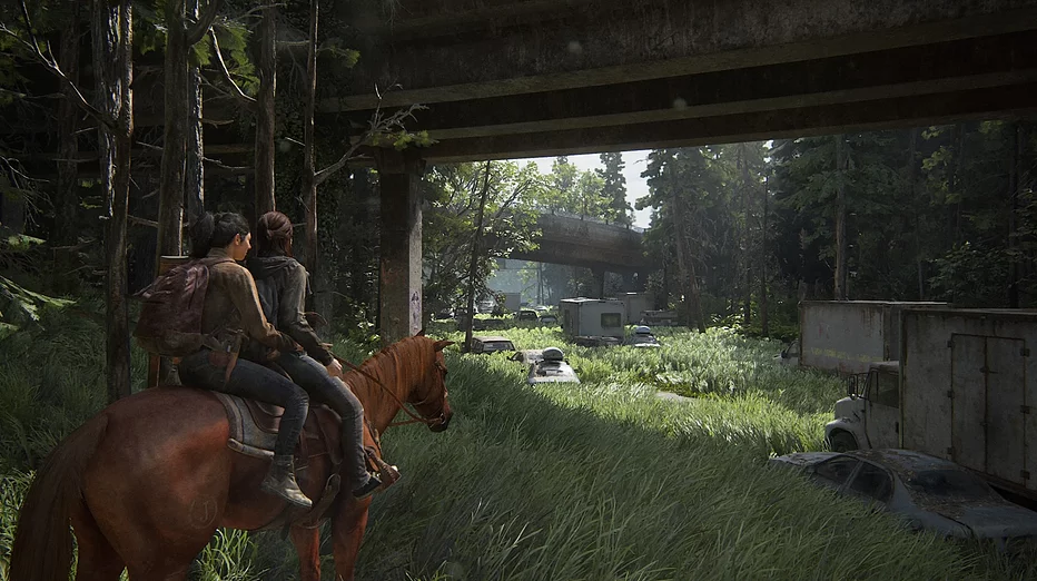 Ellie and Dina are on a brown horse walking on a road that has been totally overgrown with tall grass