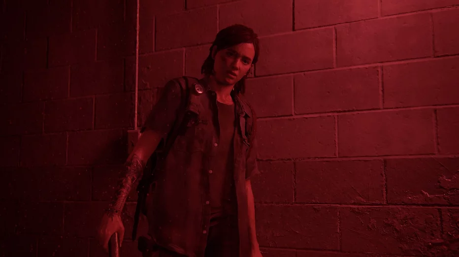 Ellie, bathed in red light, stands in a corridor looking down at something on the floor completely horrified and blank